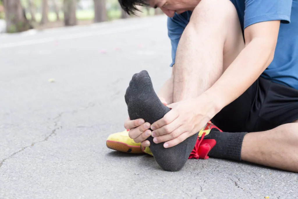 Person sitting on pavement examining foot and heel while wearing athletic sock and shoe