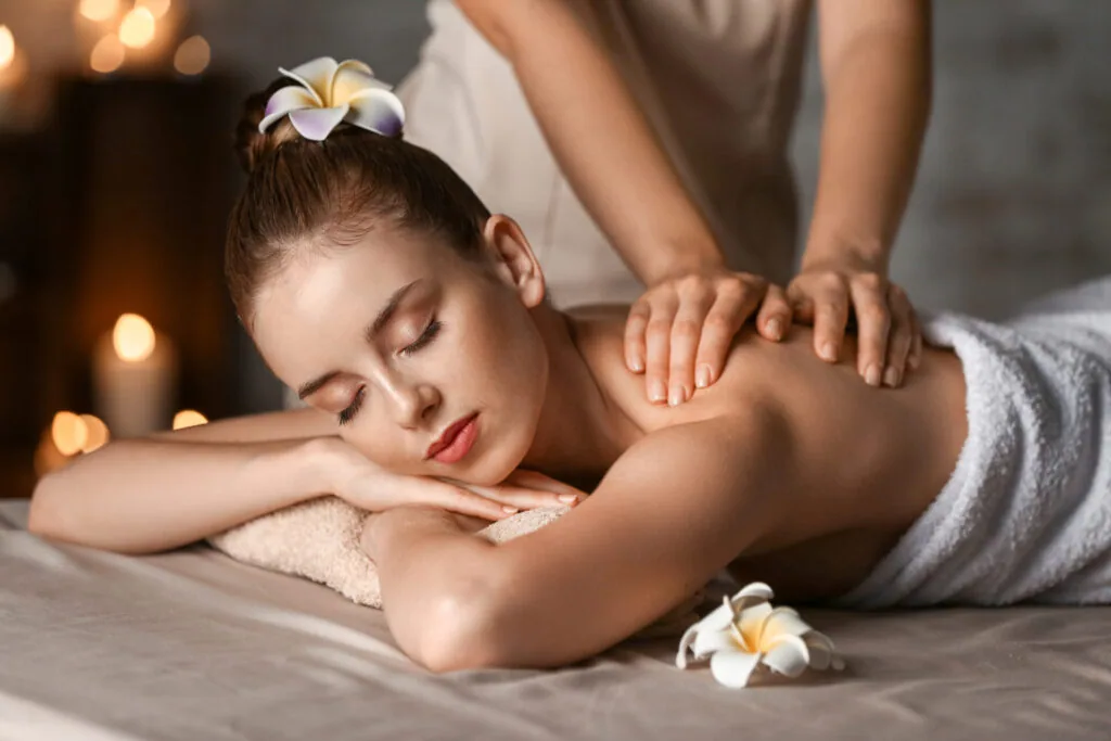 Woman receiving therapeutic shoulder massage from therapist in spa setting with white flowers and warm lighting