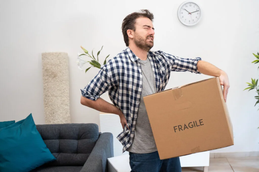 Man holding cardboard box marked fragile in living room with furniture and wall clock